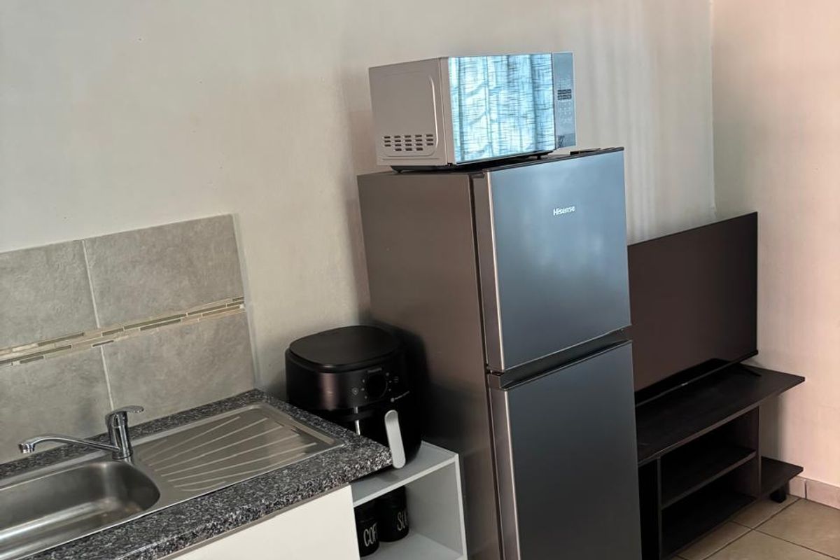 Compact kitchen area featuring a stainless steel sink, granite countertop, tiled backsplash, and ceramic floor tiles.
