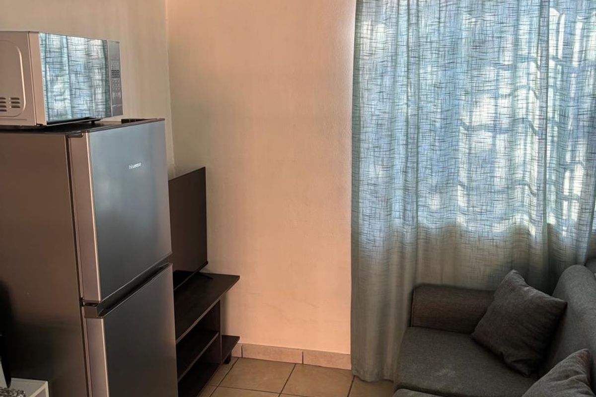 Compact open-plan living area featuring tiled flooring and a window with curtain fixtures, suitable for a small apartment layout.