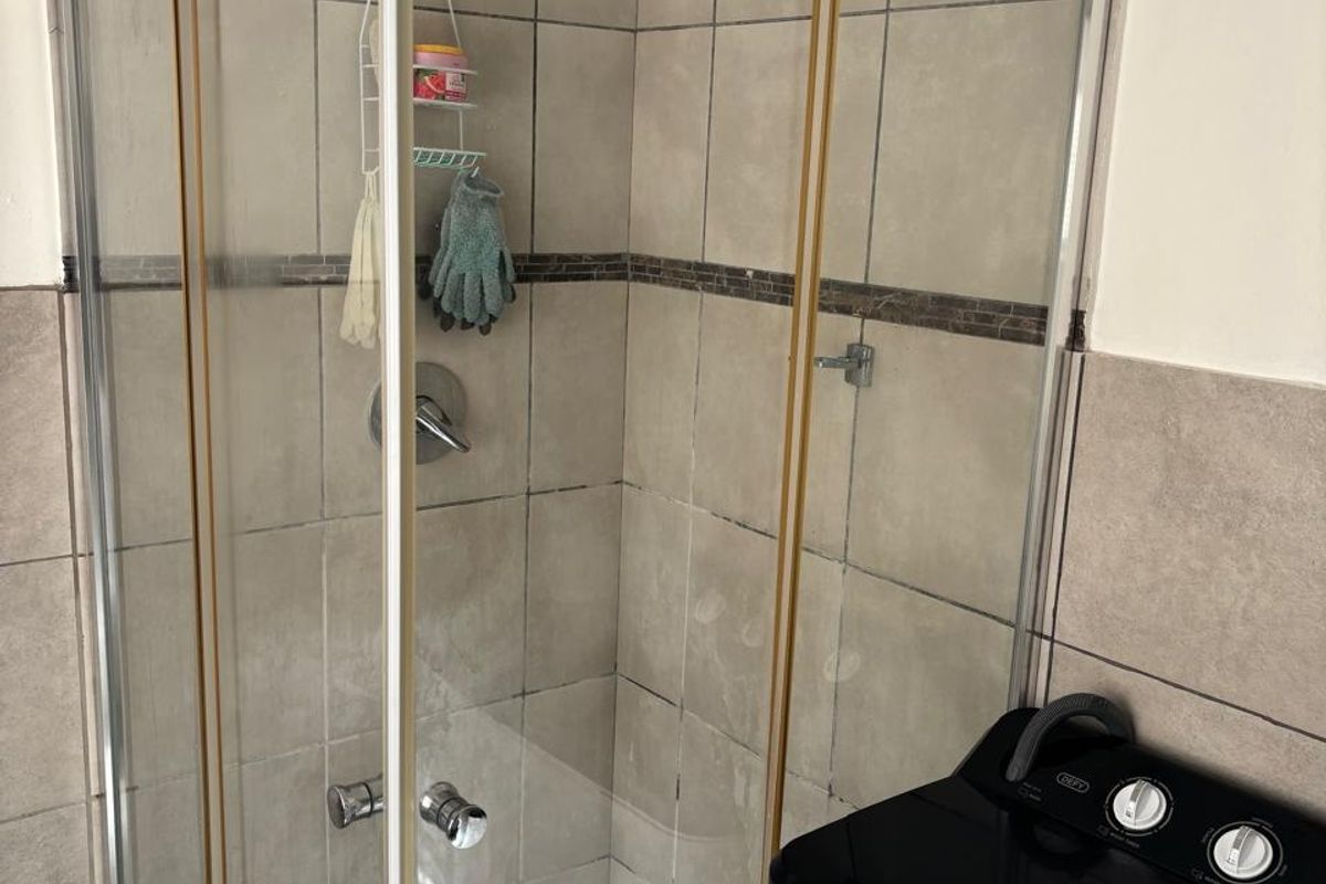 A functional bathroom featuring a corner shower enclosure with tiled walls and flooring, showing signs of wear consistent with age.