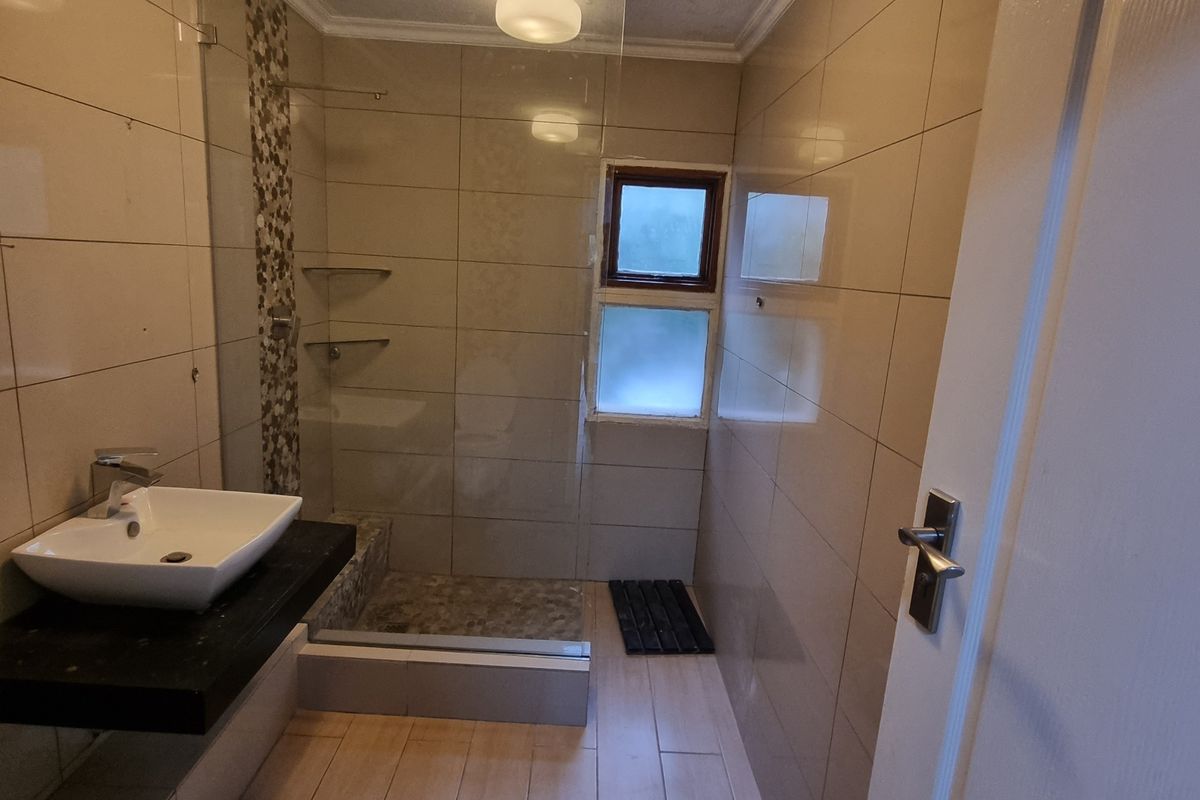 A functional bathroom featuring a walk-in shower with glass screen, modern vessel sink on a floating vanity, and neutral wall and floor tiling.