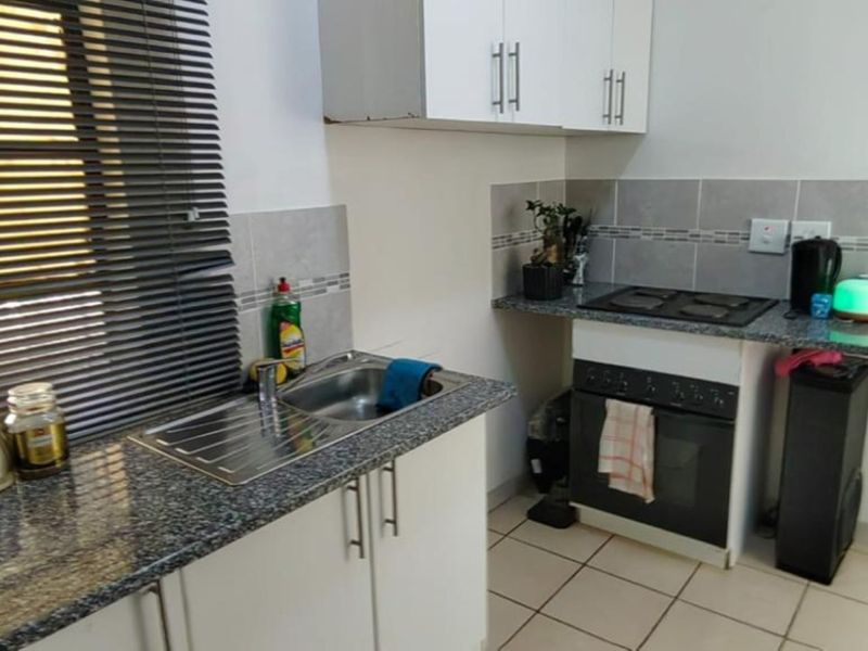 Compact kitchen featuring granite countertops, built-in oven with electric hob, tiled backsplash, and ample upper and lower cabinetry storage.