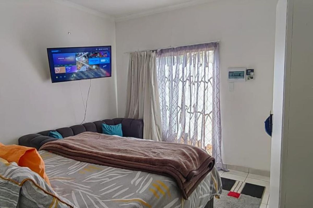 A functional bedroom featuring tiled flooring, a security gate leading to the exterior, and an integrated alarm system keypad.
