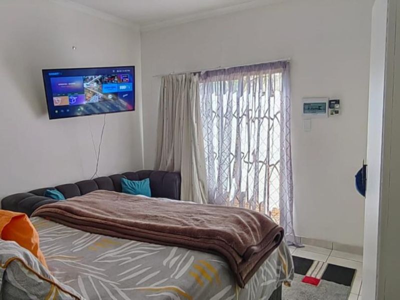 A functional bedroom featuring tiled flooring, a security gate leading to the exterior, and an integrated alarm system keypad.
