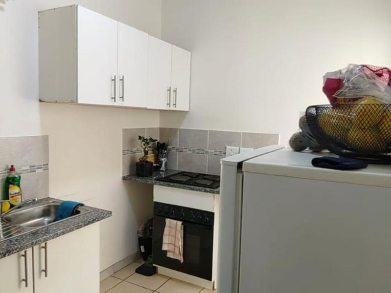 Compact kitchen featuring white cabinetry, granite countertops, tiled backsplash, and integrated oven and hob, providing a functional workspace.