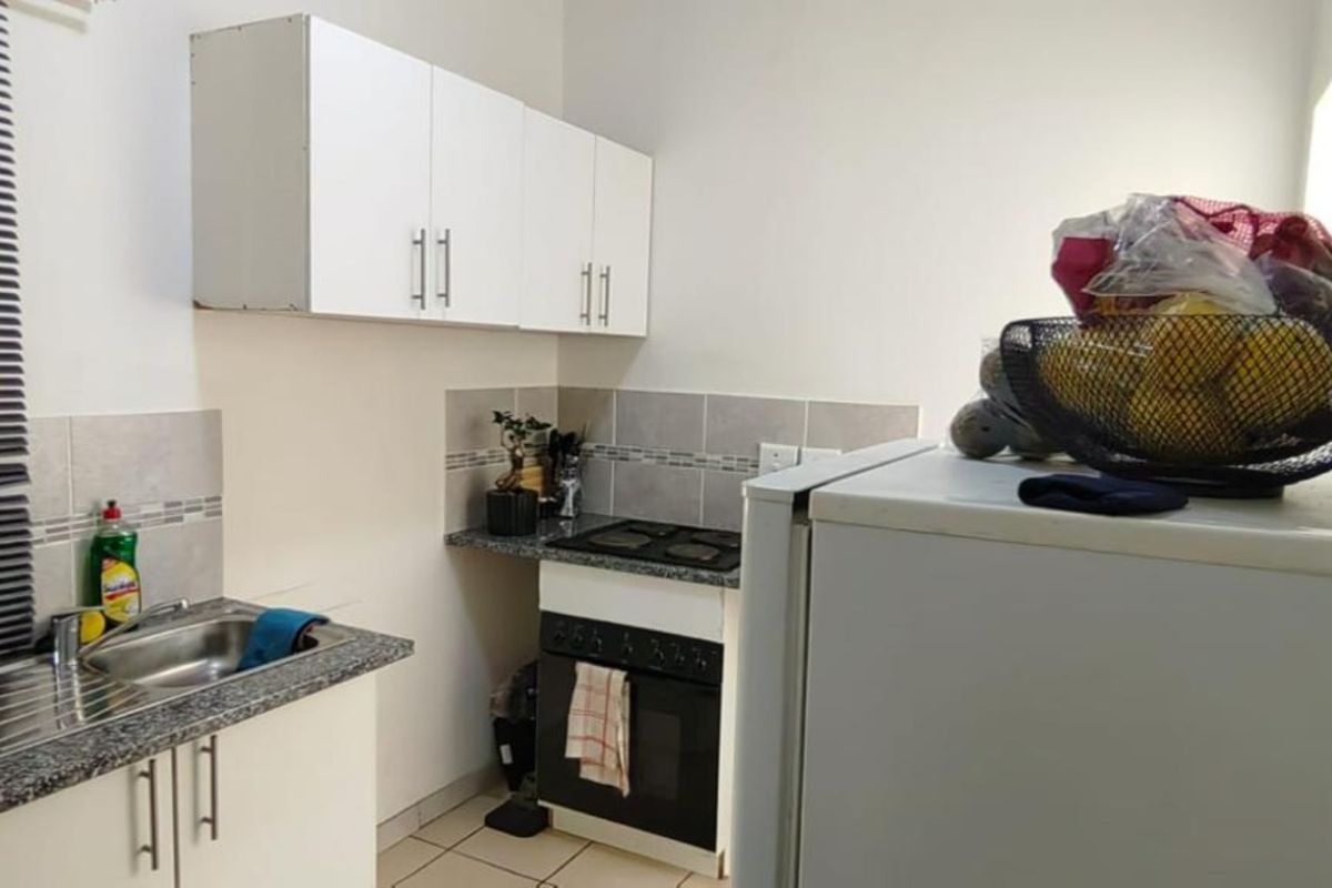 Compact kitchen featuring white cabinetry, granite countertops, tiled backsplash, and integrated oven and hob, providing a functional workspace.