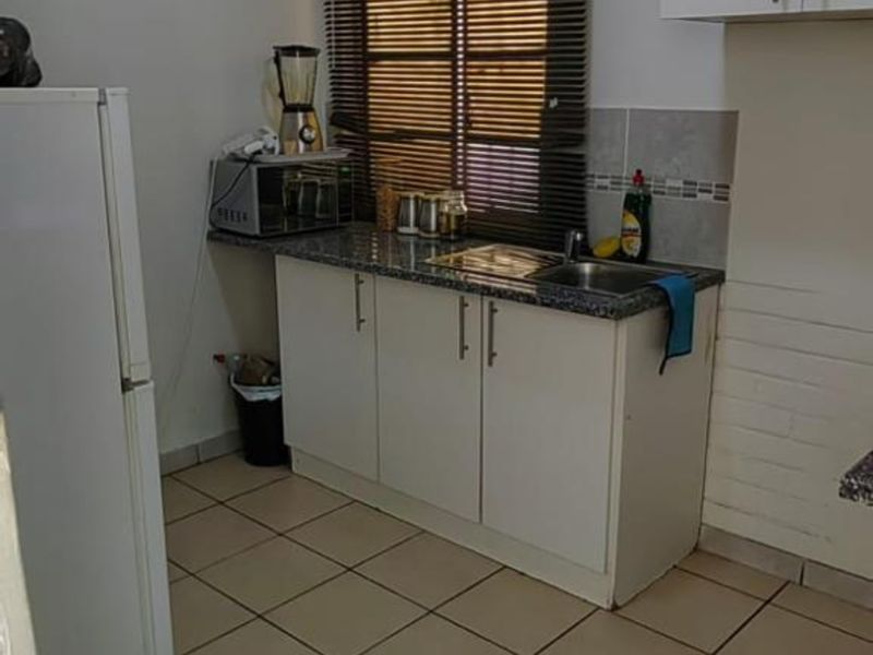 A functional kitchen featuring white built-in cabinetry, granite countertops, a stainless steel sink, and tiled flooring with a neutral backsplash.