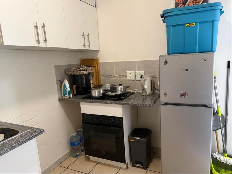 Compact kitchen featuring built-in cabinetry, granite countertops, a ceramic tile backsplash, and a built-in oven with an electric hob.