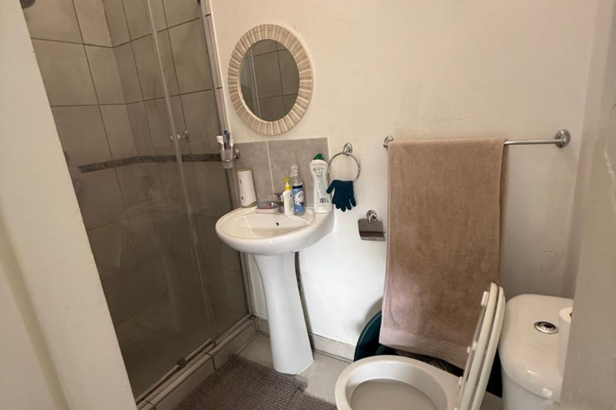 Compact bathroom featuring a pedestal basin, a glass-enclosed shower, and a standard toilet with neutral floor tiling.