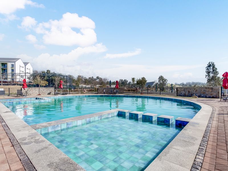 A well-maintained outdoor swimming pool area featuring a paved deck, stone boundary walls, and integrated pool steps within a landscaped complex setting.