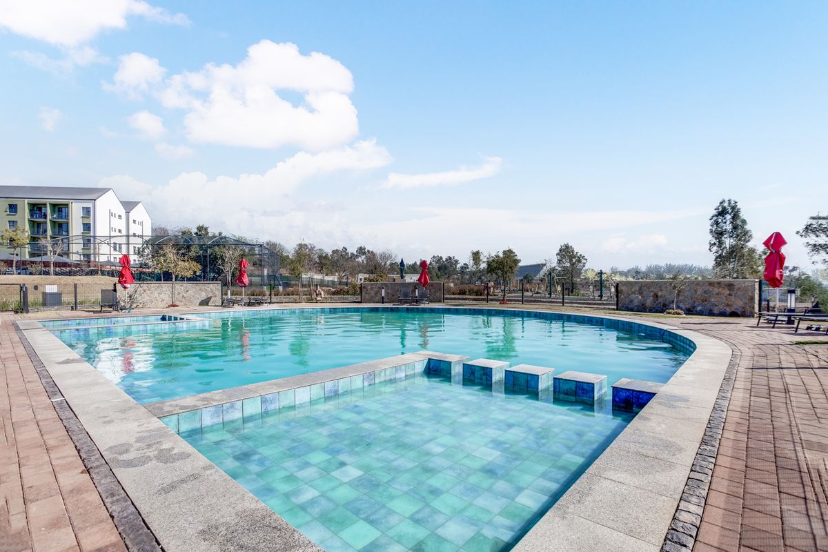 A well-maintained outdoor swimming pool area featuring a paved deck, stone boundary walls, and integrated pool steps within a landscaped complex setting.