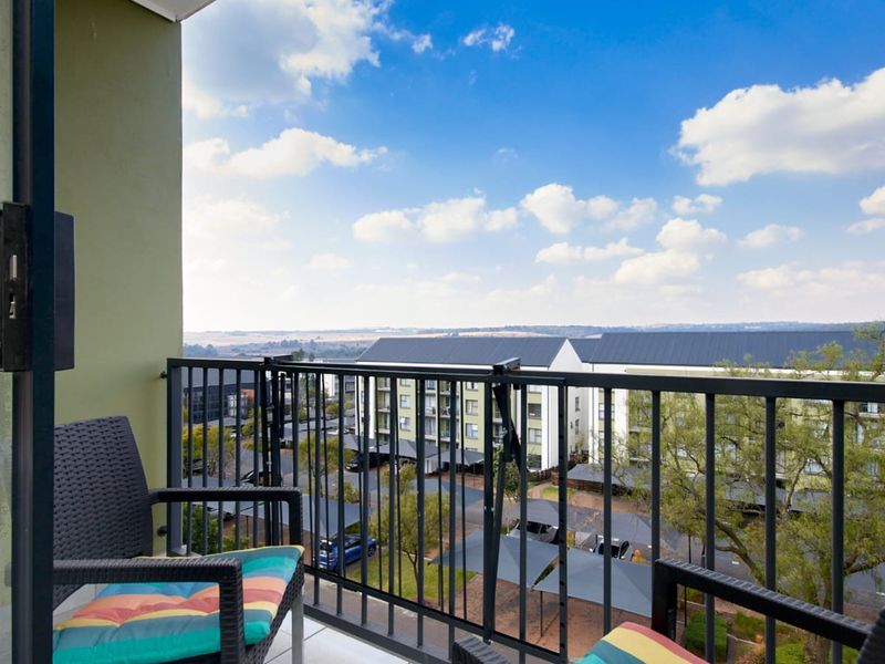 A private balcony featuring a metal balustrade and tiled flooring, offering an elevated view of the surrounding apartment complex and parking area.
