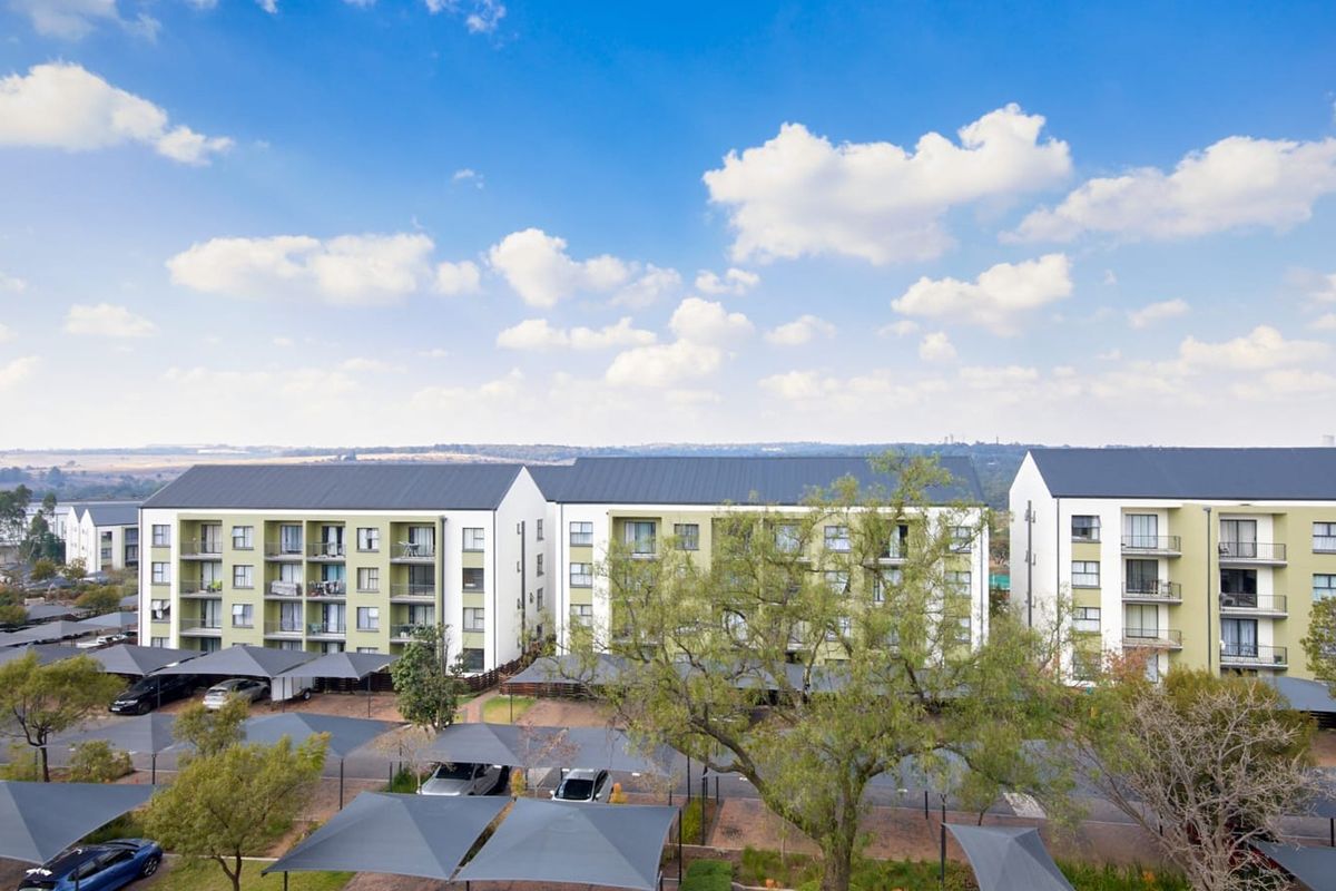 Aerial view of a modern apartment complex featuring multi-story residential blocks, private balconies, and extensive covered parking facilities within a landscaped estate.