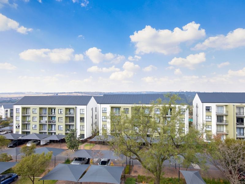 Aerial view of a modern apartment complex featuring multi-story residential blocks, private balconies, and extensive covered parking facilities within a landscaped estate.