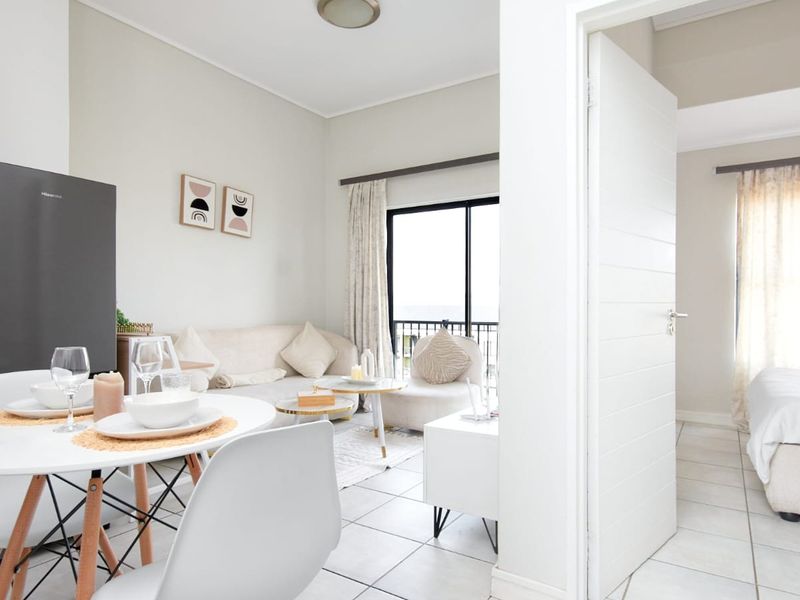 An open-plan living and dining area featuring tiled floors and a sliding door leading to a balcony, with an adjacent bedroom visible.