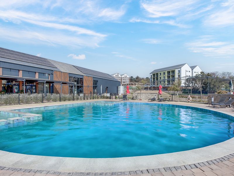 A well-maintained communal swimming pool area featuring a paved deck, modern metal fencing, and views of the surrounding apartment complex.
