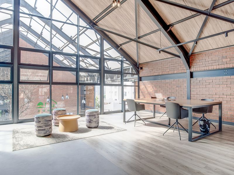 Spacious open-plan area featuring high vaulted ceilings, exposed brickwork, industrial steel beams, and expansive floor-to-ceiling windows providing abundant natural light.
