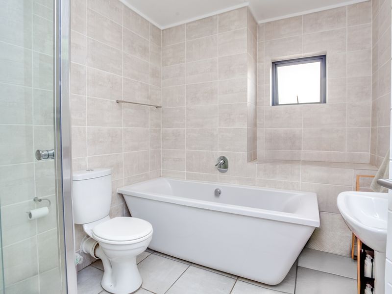 Modern bathroom featuring a freestanding bathtub, separate glass shower enclosure, pedestal basin, and neutral floor-to-ceiling tiling.