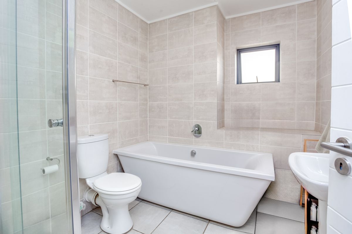 Modern bathroom featuring a freestanding bathtub, separate glass shower enclosure, pedestal basin, and neutral floor-to-ceiling tiling.