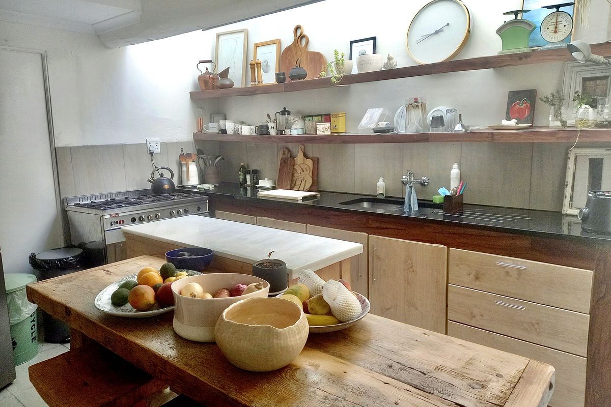 A functional kitchen featuring wooden cabinetry, dark stone countertops, open shelving, and a built-in gas stove with an integrated prep island.