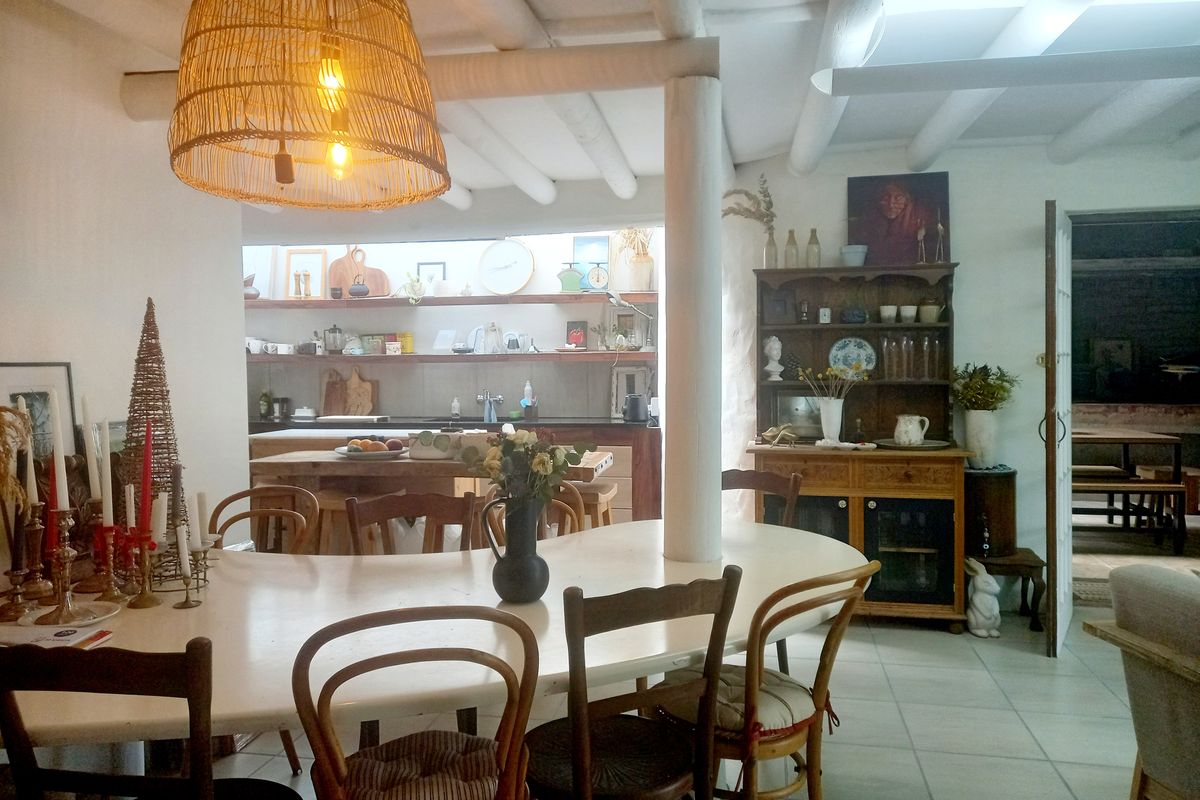 An open-plan living and dining area featuring exposed white timber ceiling beams, tiled flooring, and a functional kitchen with open shelving.