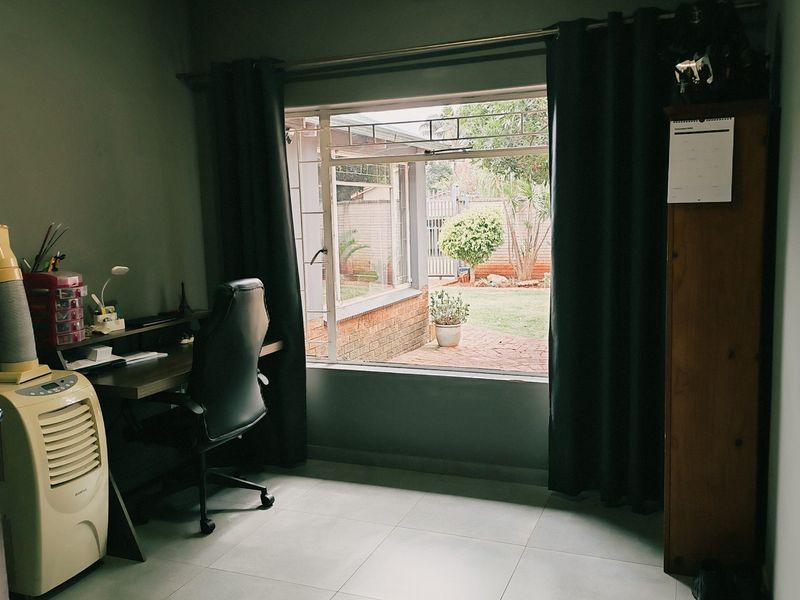 A functional home office space featuring large windows with garden views and neutral tiled flooring.