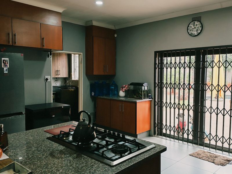 A functional kitchen featuring granite countertops, built-in cabinetry, and a gas hob, with direct access to the outdoor area through a security-gated sliding door.