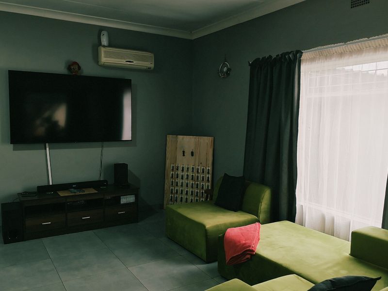 A living room featuring tiled flooring, a wall-mounted air conditioning unit, and large windows with curtains.
