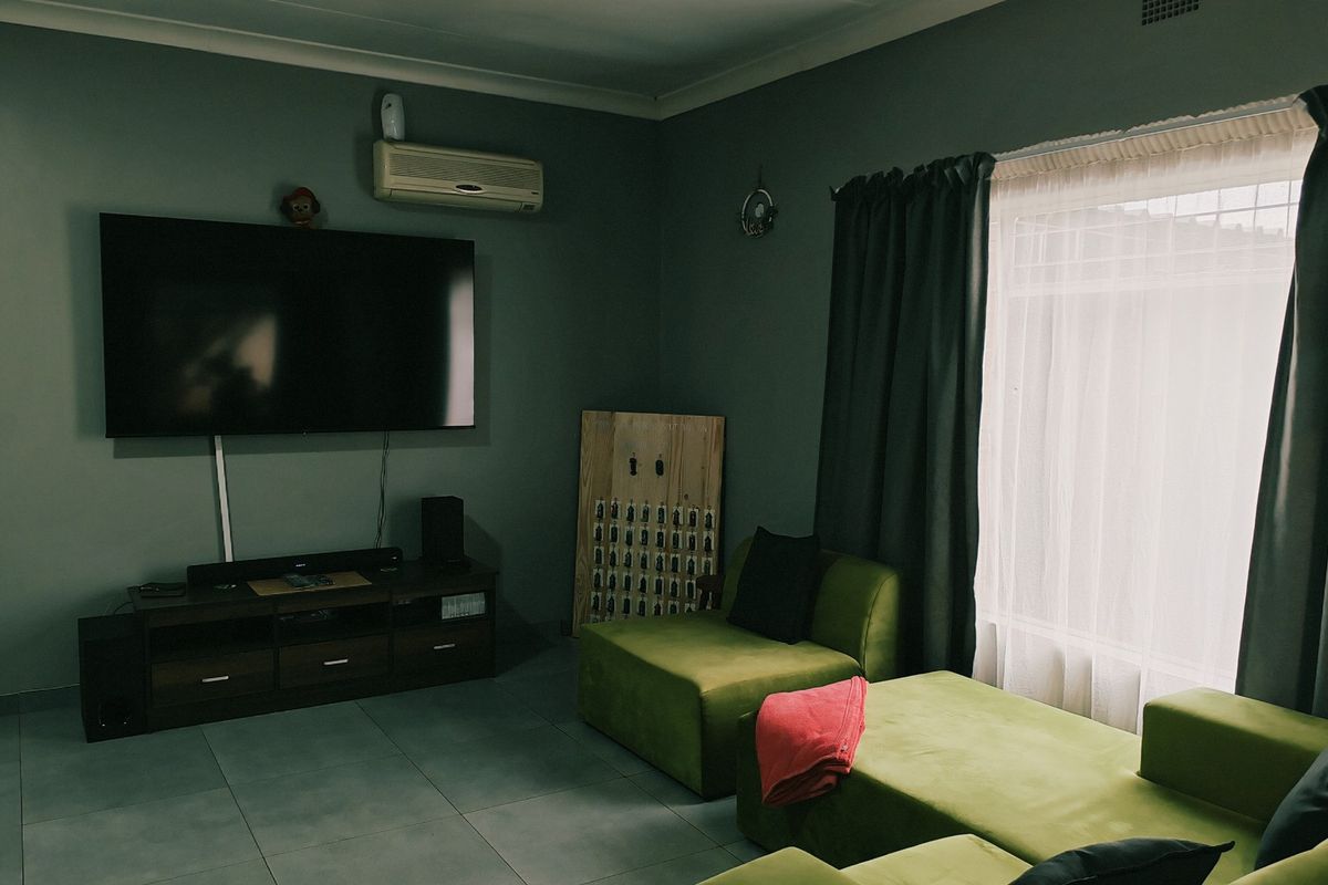 A living room featuring tiled flooring, a wall-mounted air conditioning unit, and large windows with curtains.