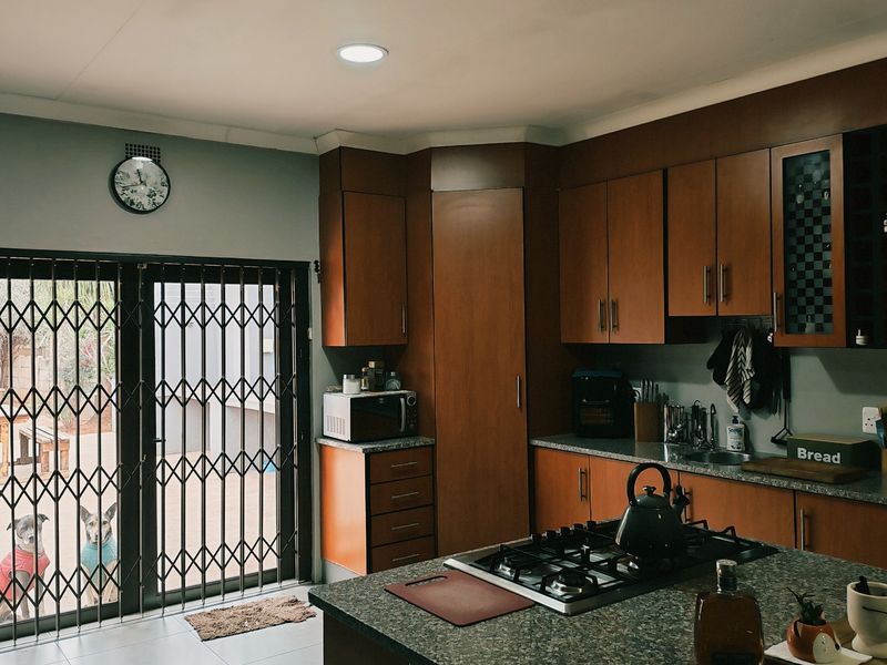 A functional kitchen featuring wood-finish cabinetry, granite countertops, a central gas hob, and direct access to the outdoor patio area through a security gate.