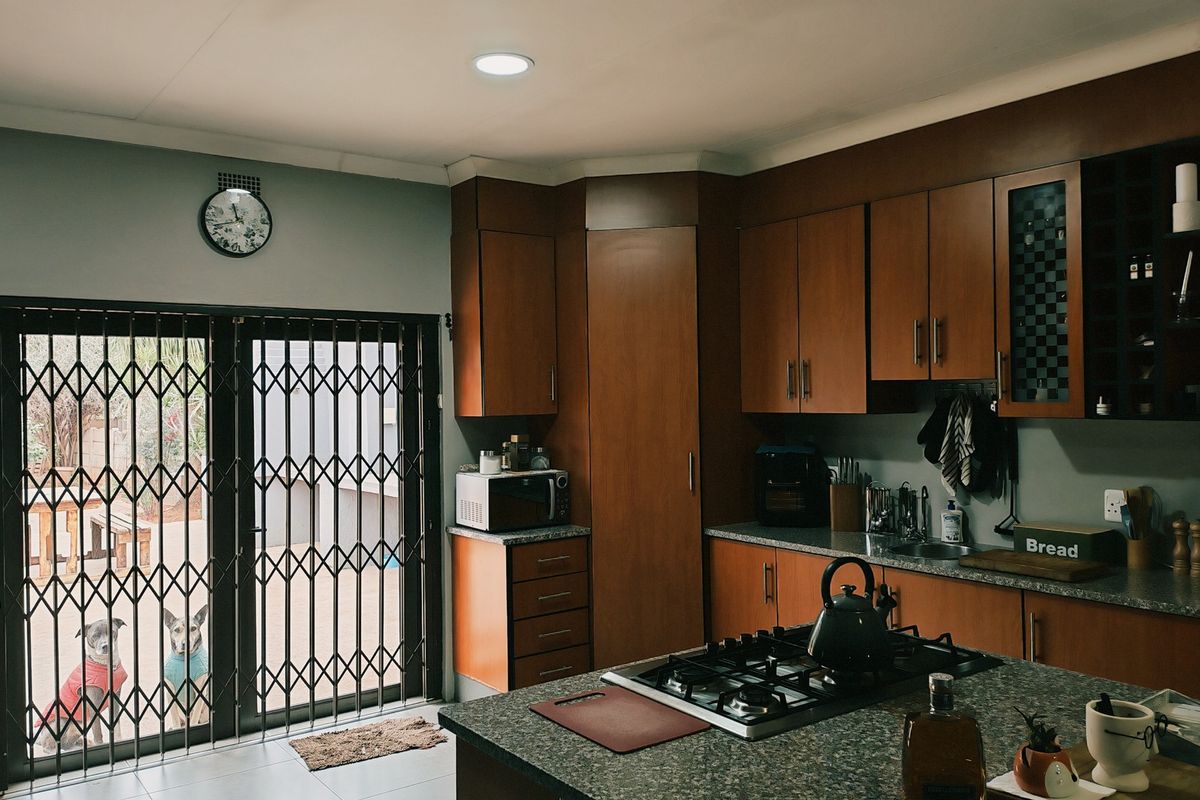 A functional kitchen featuring wood-finish cabinetry, granite countertops, a central gas hob, and direct access to the outdoor patio area through a security gate.