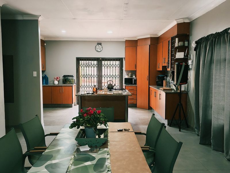 Open-plan kitchen and dining area featuring wooden cabinetry, granite countertops, a central island, and tiled flooring with access to the exterior.