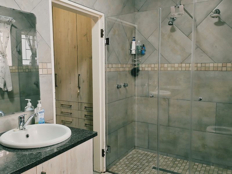 A well-appointed bathroom featuring a granite-topped vanity, a spacious glass-enclosed shower with dual shower heads, and convenient built-in storage cupboards.