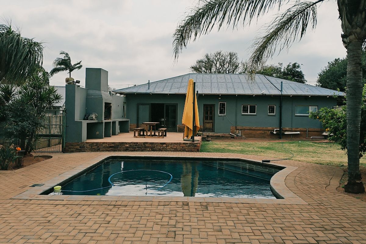 Rear view of the property featuring a swimming pool, paved patio area, and a built-in outdoor braai facility.