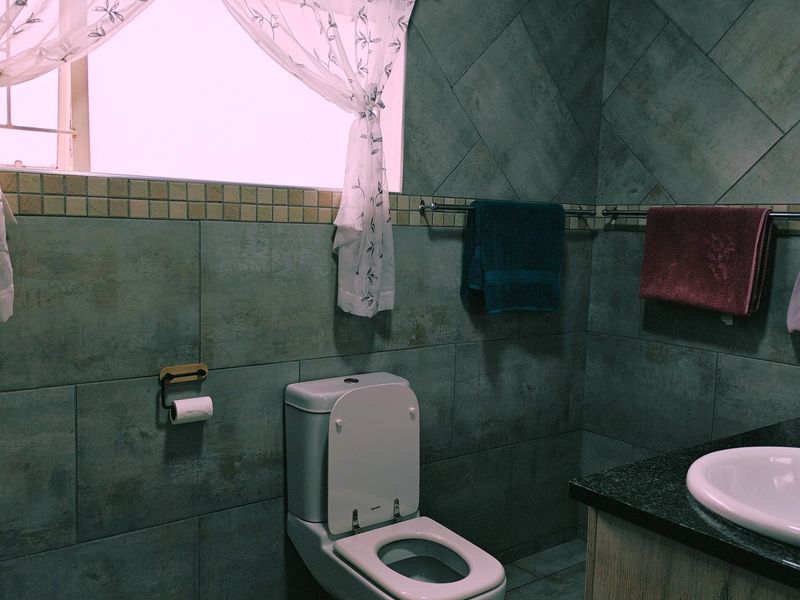 A functional bathroom featuring dark grey wall tiles, a built-in vanity with a basin, and a standard toilet.