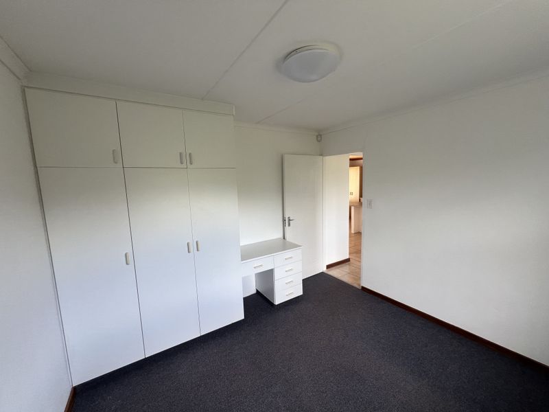 A clean, empty bedroom featuring built-in cupboards, a matching built-in desk, and dark carpeting, offering a neutral space ready for personalization.