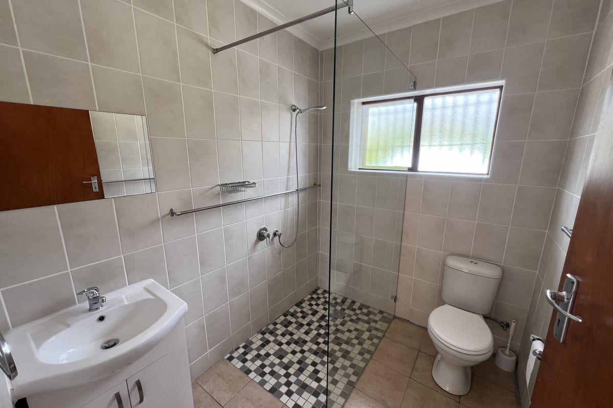 A clean, functional bathroom featuring a walk-in shower with a glass screen, vanity basin, and toilet, finished with neutral wall and floor tiling.