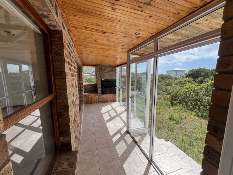 Enclosed patio featuring a built-in braai, timber-clad ceiling, tiled flooring, and large aluminium sliding doors offering views of the surrounding garden.