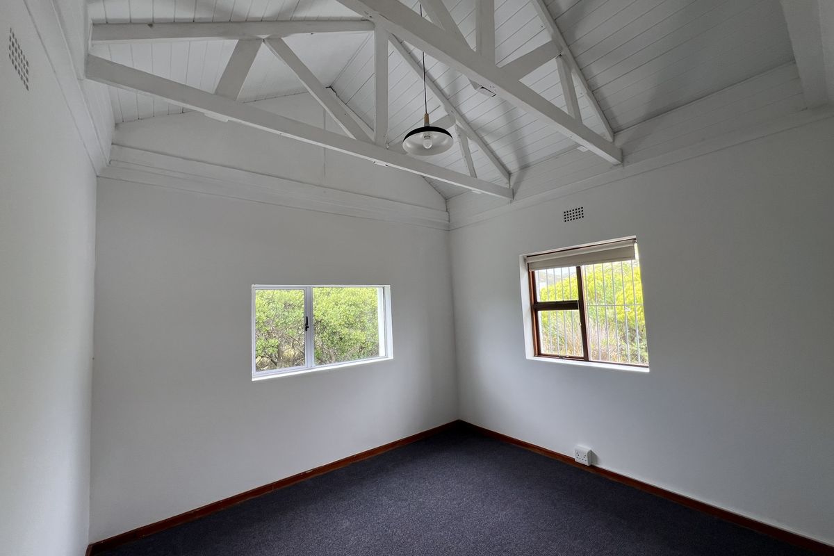 A bright, empty bedroom featuring a high vaulted ceiling with exposed white timber trusses, carpeted flooring, and dual windows with security bars.