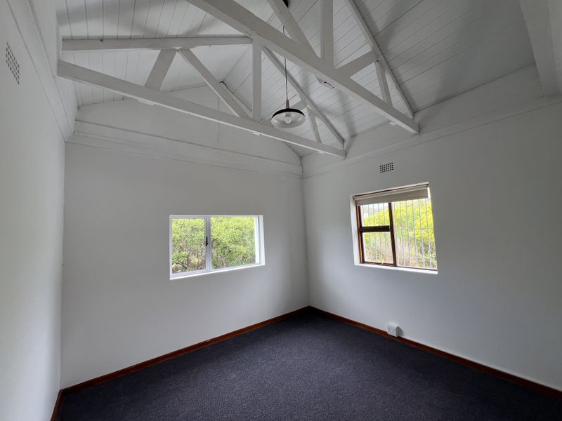 A bright, empty bedroom featuring a high vaulted ceiling with exposed white timber trusses, carpeted flooring, and dual windows with security bars.