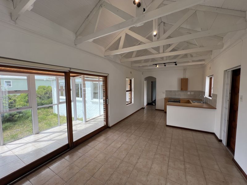 Open-plan living and kitchen area featuring high vaulted ceilings with exposed timber trusses, tiled flooring, and large sliding doors leading to an outdoor space.