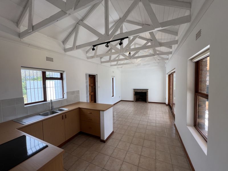 Spacious open-plan living area featuring a vaulted ceiling with exposed trusses, a built-in fireplace, and a functional kitchen with laminate cabinetry.