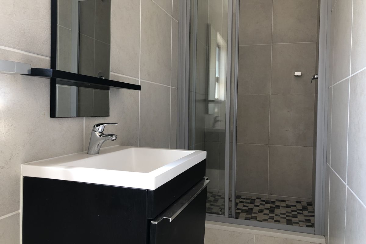 Modern bathroom featuring a sleek vanity with basin, wall-mounted mirror, and a glass-enclosed shower with tiled flooring.