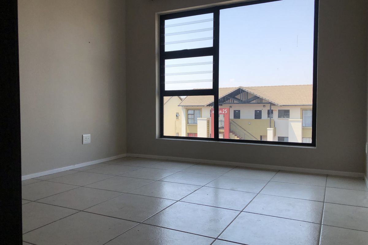 An empty bedroom featuring neutral tiled flooring, a large window with black framing, and a curtain rod, offering a clean and versatile living space.