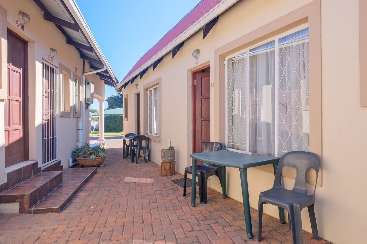 A paved outdoor walkway between apartment units featuring security gates, external lighting, and tiled entrance steps.