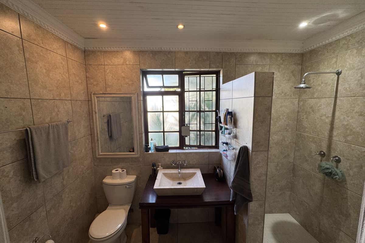A bathroom featuring a walk-in shower with a rainfall showerhead, a vessel sink on a wooden vanity, and tiled walls.