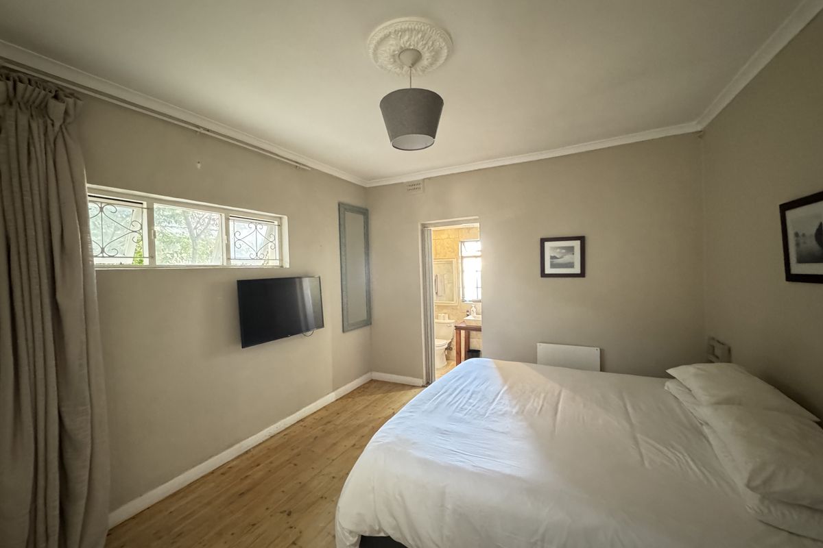 A bedroom featuring timber flooring, a ceiling rose, and an en-suite bathroom access point.