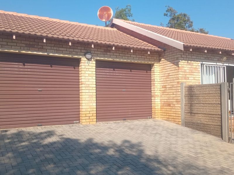 Front view of a townhouse featuring a double garage with roll-up doors, facebrick exterior, tiled roof, and a paved driveway.