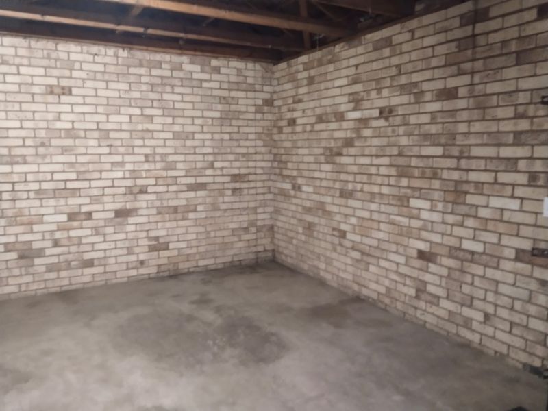 An unfinished garage space featuring exposed brick walls, a concrete floor, and exposed timber ceiling joists, offering a blank canvas for storage or workshop use.