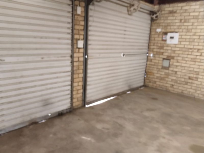 A double garage featuring face brick walls, concrete flooring, and two roller doors showing signs of wear.