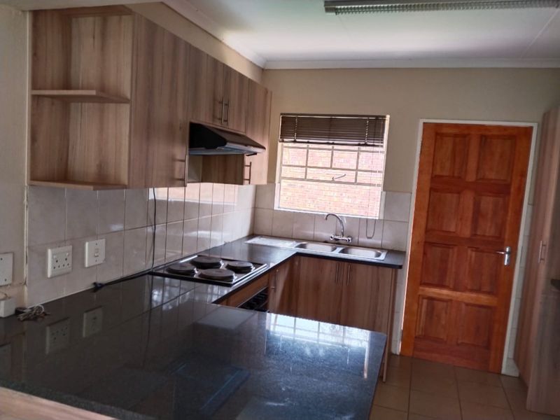 A functional kitchen featuring laminate cabinetry, granite countertops, an electric hob with extractor fan, and a double sink with tiled backsplash.